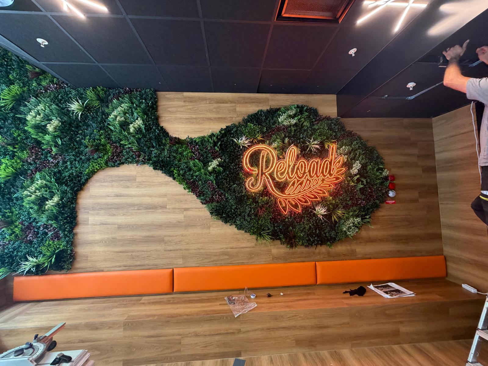 Orange neonskylt med texten Reload monterad på växtvägg i restaurang